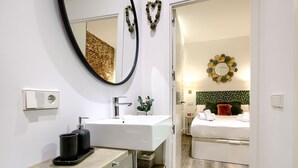 Un bagno moderno con un lavandino bianco, uno specchio e un water. Si nota un cestino e un portasciugamani. Il bagno presenta un pavimento in legno e pareti bianche.