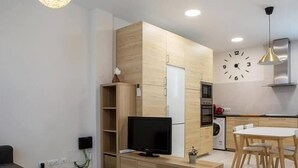 Ein modernes Wohnzimmer mit Fernseher, Holzmöbeln, einem Essbereich und einer Küche mit Geräten.