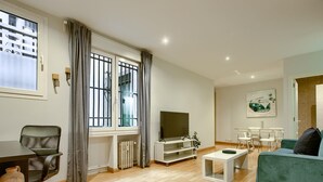 A modern living room with a wooden floor, a green sofa, a TV, a dining area with chairs, and a radiator. - Callao Central - Renovated and Central Apartment (Madrid)