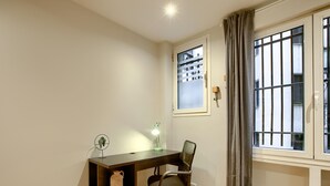 A room with a wooden desk, a chair, a lamp, a shelf with a vase, and a window with curtains. - Callao Central - Renovated and Central Apartment (Madrid)