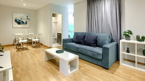 A modern living room with a grey sofa, white coffee table, and a dining area with chairs and a glass table. - Callao Central - Renovated and Central Apartment (Madrid)
