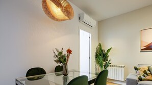 Ein moderner Essbereich mit einem Glastisch, grünen Stühlen, einer dekorativen Vase mit Blumen und einer Hängelampe.