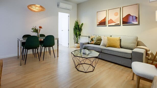 Ein modernes Wohnzimmer mit einem grauen Sofa, einem Glastisch und einem Essbereich mit einem weißen Tisch und grünen Stühlen.