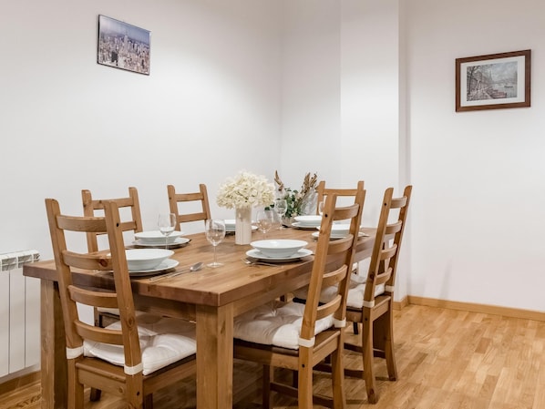Un comedor con una mesa de madera dispuesta para seis personas, rodeada de sillas de madera con cojines blancos.
