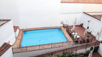 Una piscina en la azotea con barandilla metálica, rodeada de plantas en macetas y mobiliario de exterior.