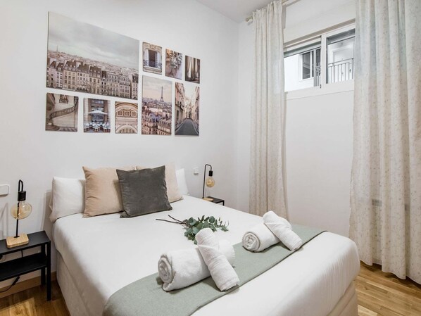 Ein Hotelzimmer mit Bett, Nachttisch, Lampe und einem Fenster mit Vorhängen.