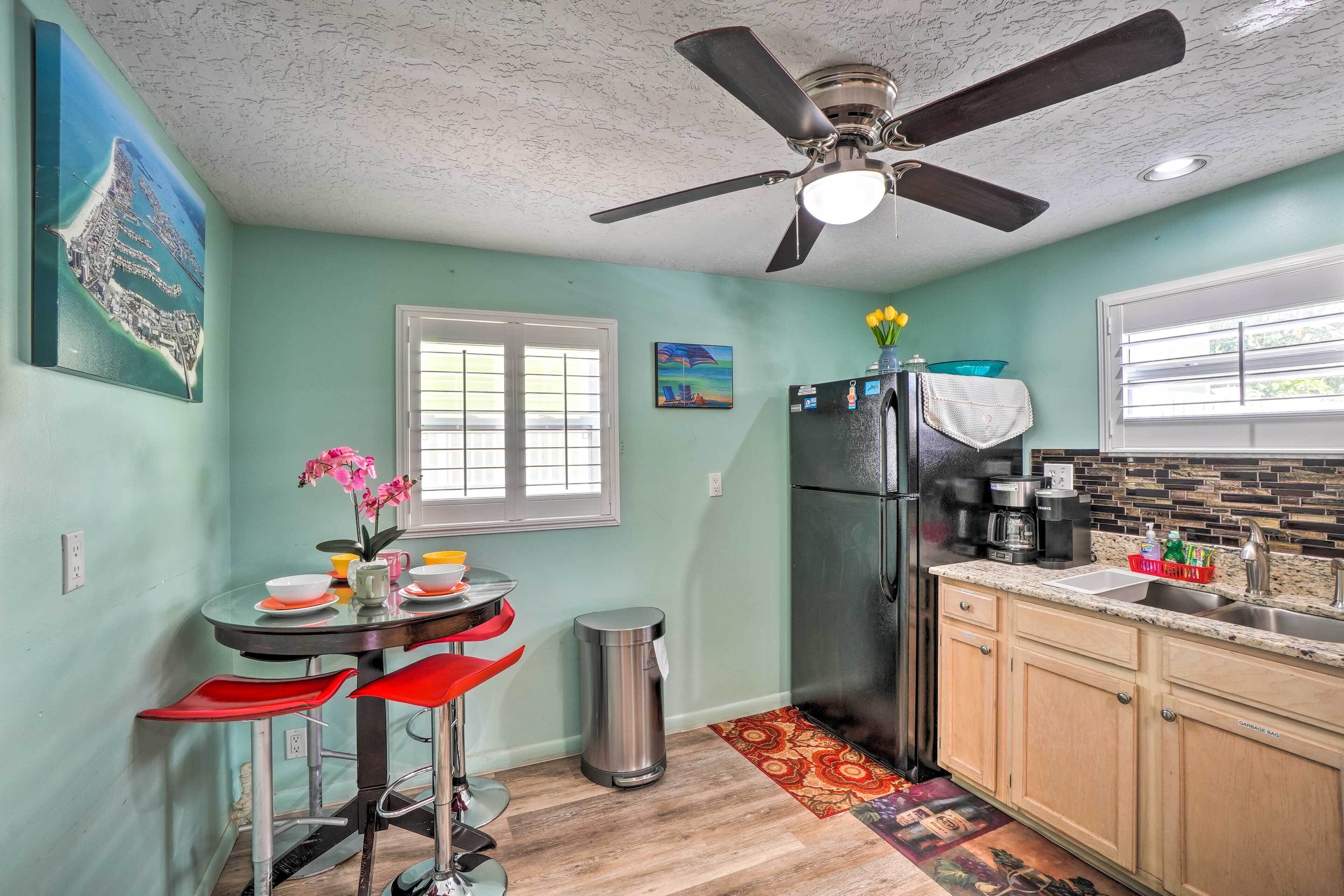 A kitchen with a ceiling fan, a refrigerator, a sink, and a dining area with red chairs.