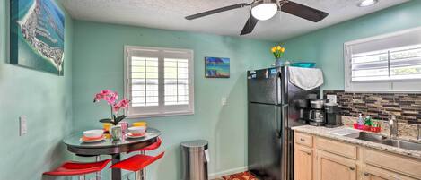 A kitchen with a ceiling fan, a refrigerator, a sink, and a dining area with red chairs.