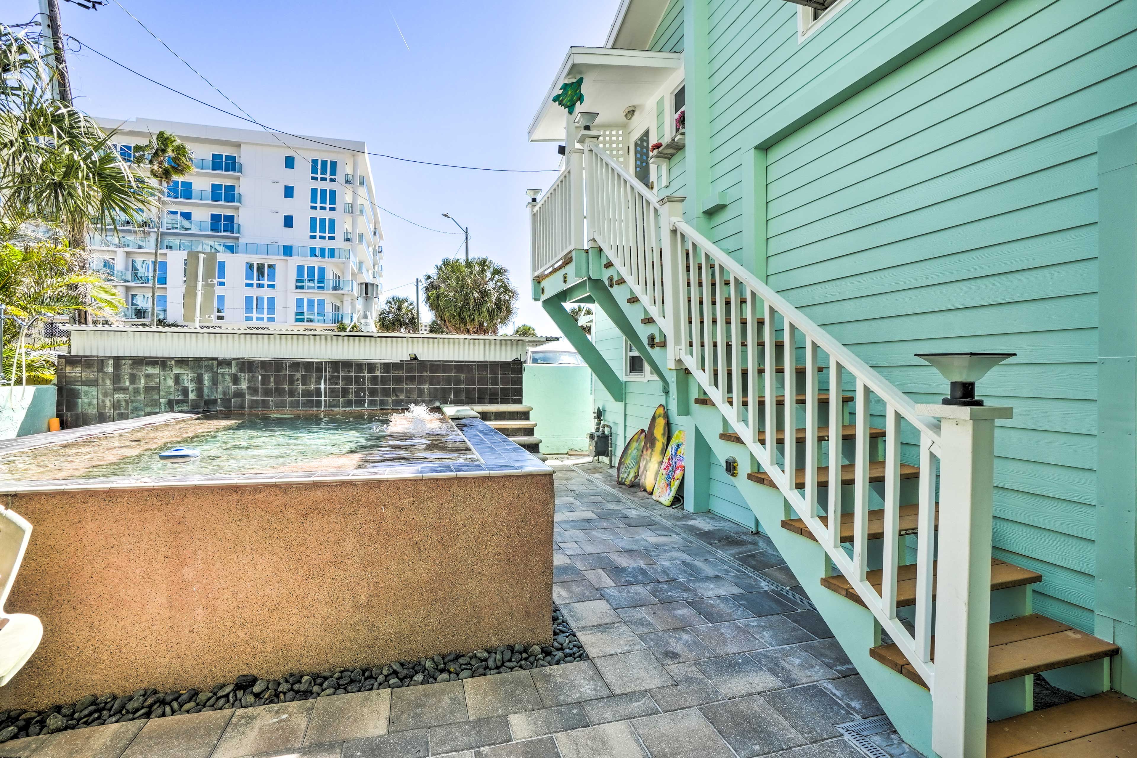 A hot tub with a stone surround, a staircase with a railing, and a building with a light blue exterior in the background.