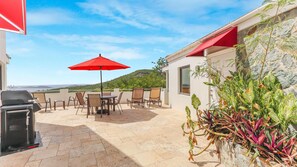 An outdoor patio with a barbecue grill, a table with chairs, and a red umbrella.