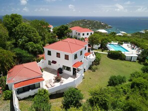 A white building with a red roof, a swimming pool, and a view of the sea.