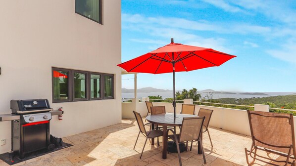 A patio with a grill, table, chairs, and a red umbrella.