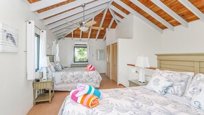 A bedroom with two beds, a ceiling fan, a window with curtains, and a view of greenery outside.