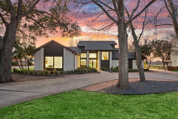 A modern house with a driveway, a lawn, and trees.