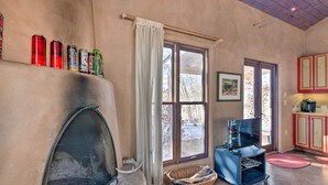 A cozy living room with a fireplace, a television, and a window with a view of trees.