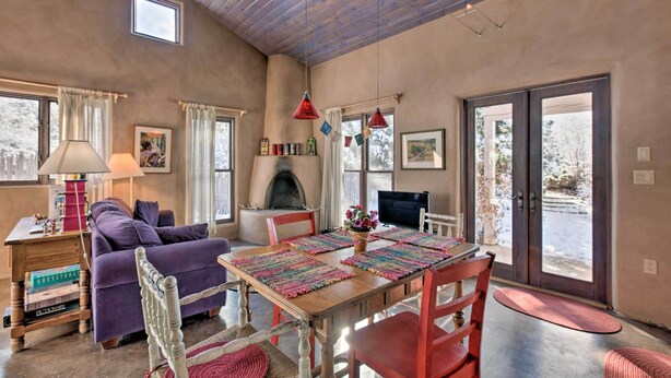 A cozy living room with a fireplace, wooden ceiling, and large windows.