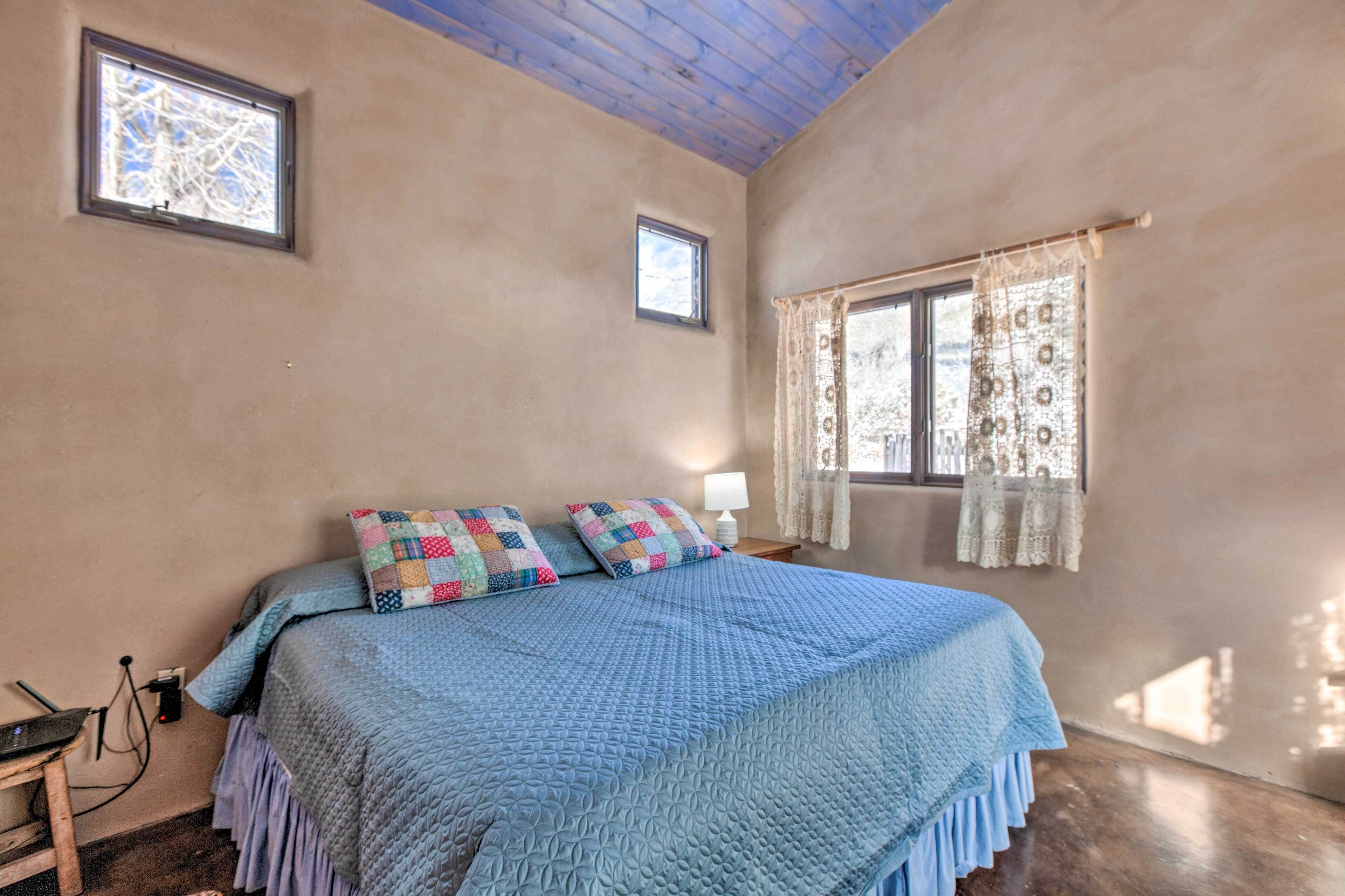 A bedroom with a large bed, two windows, and a wooden ceiling.