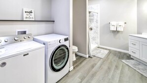 A modern laundry room with a front-loading washer and dryer, a toilet, and a shower area.