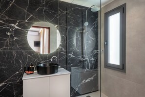 Ein modernes Badezimmer mit einem schwarzen Marmorwaschbecken, einem runden Spiegel und einer Duschkabine aus Glas.