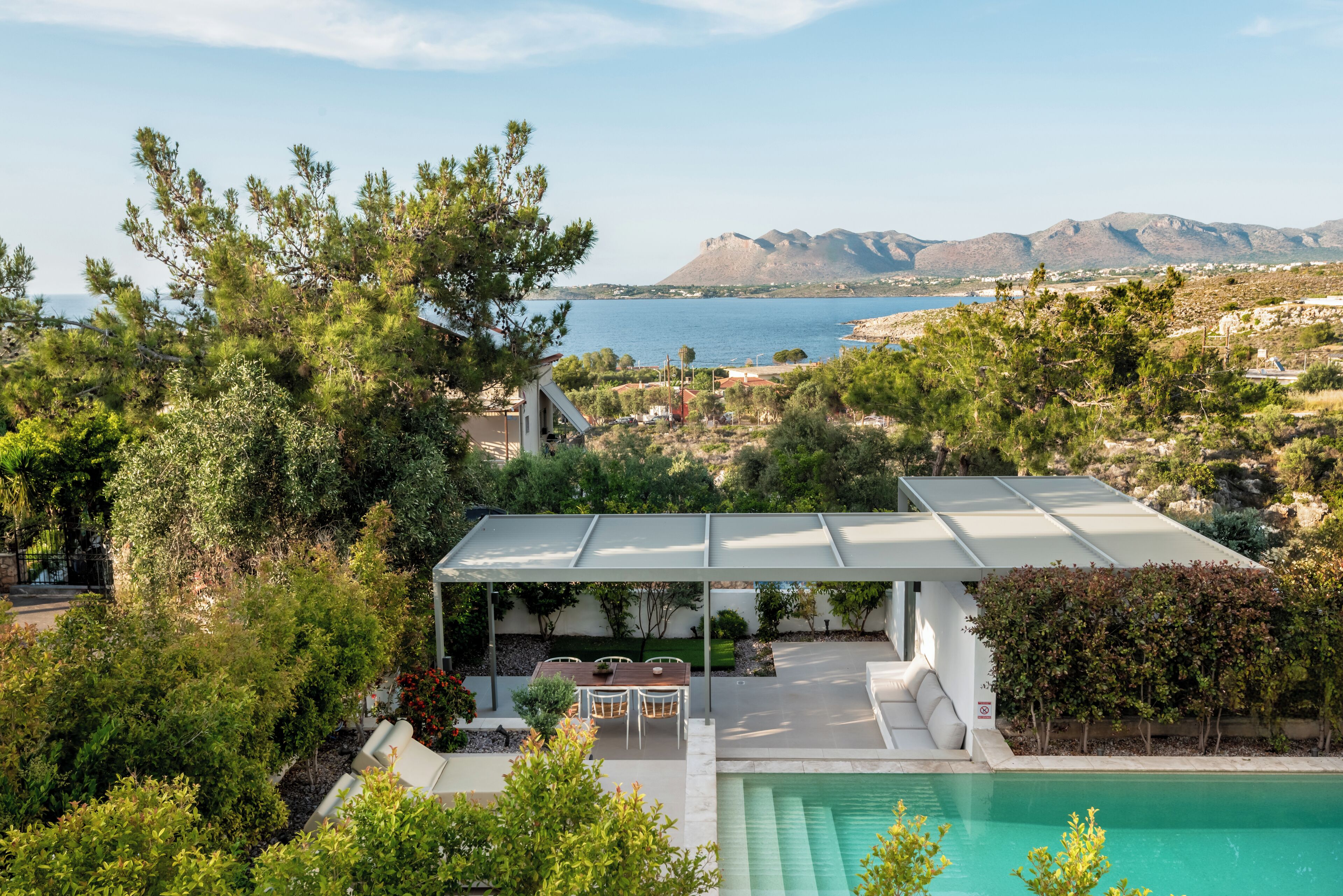 A modern outdoor patio with a pool, surrounded by lush greenery and overlooking a scenic lake and mountains.