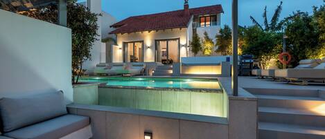 A modern outdoor pool area with a covered seating area, a staircase leading to a house, and a barbecue setup.