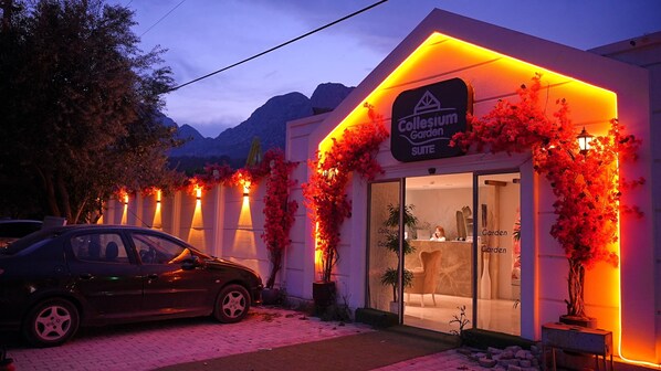 A hotel entrance with a sign reading "Collesium Garden Suite," surrounded by red flowering plants and a mountain backdrop. - Collesium Garden (Konyaalti)