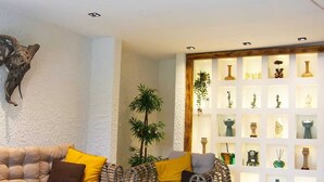 A modern living room with a sofa set, a glass coffee table, and wicker chairs. There is a wall-mounted shelf with decorative items.