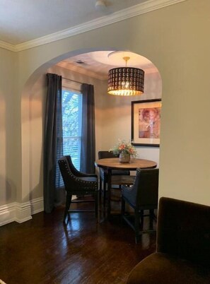 Enjoy meals in this cozy dining area with a round table and two chairs, surrounded by a decorative light fixture and a beautiful window with curtains.