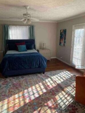 Un dormitorio con cama, ventilador de techo, ventana con cortinas y puerta.