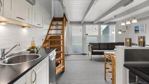 A modern kitchen with a wooden staircase, a dining area with a black sofa, and a view of the outside through a glass door. - Nice apartment in Hemmet with sauna (Hemmet)