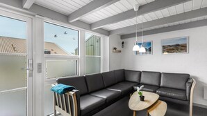 A modern waiting area with a black leather sofa, a small wooden table with a plant, and a bench with a blue towel. - Nice apartment in Hemmet with sauna (Hemmet)