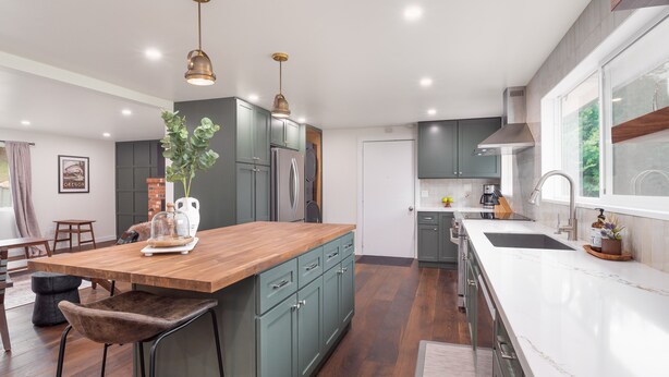 Una cucina moderna con isola in legno, mobili verdi, elettrodomestici in acciaio inossidabile e illuminazione a sospensione.