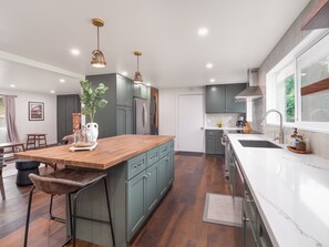 A modern kitchen with a wooden island, green cabinets, stainless steel appliances, and pendant lighting. - Singing Waters at N. Umpqua (Roseburg North)