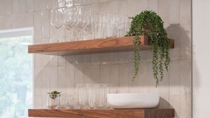 Una cucina con mensole in legno che contengono bicchieri e una pianta, una ciotola bianca e un tagliere di legno.