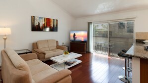 Una sala de estar moderna con sofá, mesa de centro, televisor y un balcón con sillas.