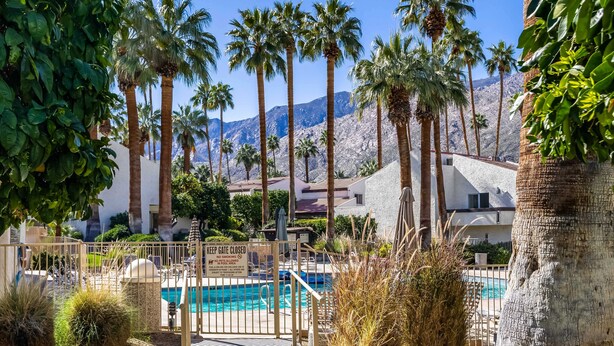 Zona de piscina con una cerca cerrada, palmeras y montañas al fondo.