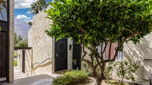 Un edificio con fachada de piedra, una puerta negra y un pequeño jardín con un árbol y arbustos.