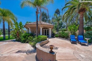 Relax in a serene patio area with a gazebo and lounge chairs, surrounded by lush greenery and palm trees.