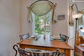 Enjoy meals in this cozy dining area with a table for two, a wall-mounted lamp, and a view of lush greenery outside.