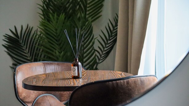 Une chaise moderne, une bouteille de vin et un diffuseur d’arômes décoratif en forme de roseau, le tout posé sur une table ronde.