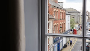 Une vue à travers une fenêtre donnant sur une rue, avec des immeubles, une cabine téléphonique rouge et une enseigne de pharmacie.