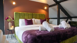 Un lit bien fait, avec une tête de lit verte, une literie blanche et violette, et deux serviettes blanches posées sur le lit.