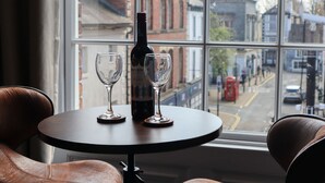 Une table avec une bouteille et deux verres, une fenêtre donnant sur des immeubles et une cabine téléphonique rouge à l’extérieur.