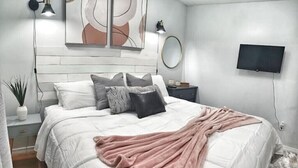 Ein Schlafzimmer mit einem Bett, einem an der Wand montierten Fernseher und einem Nachttisch mit einer Lampe.