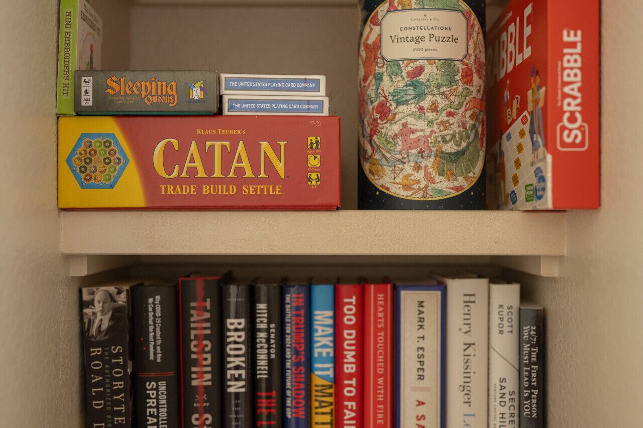 Una estantería con varios libros y juegos, incluyendo 'Catan', 'Sleeping Queens' y 'Scrabble'.