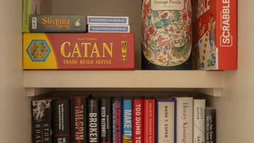 Una estantería con varios libros y juegos, incluyendo 'Catan', 'Sleeping Queens' y 'Scrabble'.