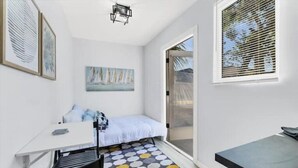 A small, bright room with a bed, a desk, and a window with blinds. - Tropical Tiny house with Outdoor jacuzzi & Gazebo (Tampa)