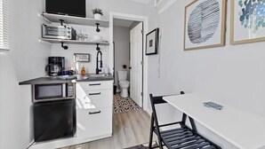 A compact kitchen with white cabinetry, a microwave, a coffee maker, and a small dining table with chairs. - Tropical Tiny house with Outdoor jacuzzi & Gazebo (Tampa)