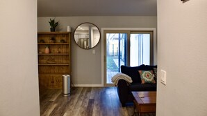 A living room with a wooden floor, a black sofa, a coffee table, a bookshelf, a mirror, and a sliding glass door leading outside. - Chill Suburban Get Away (Corpus Christi)