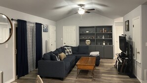 A living room with a dark blue sofa, a wooden coffee table, and a ceiling fan. - Chill Suburban Get Away (Corpus Christi)